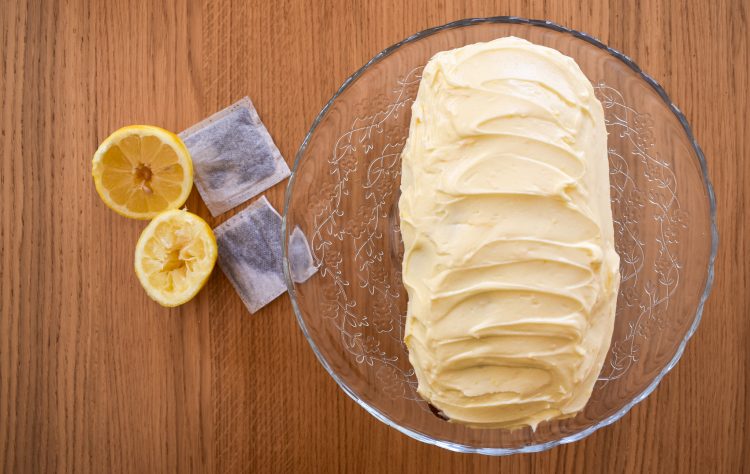Top shot of earl grey and lemon cake on glass stand. Lemons and teabags to the side. 
