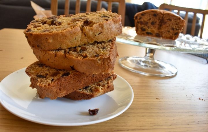 Earl Grey Tea Loaf slices stacked on a plate. Rest of cake on stand in background.