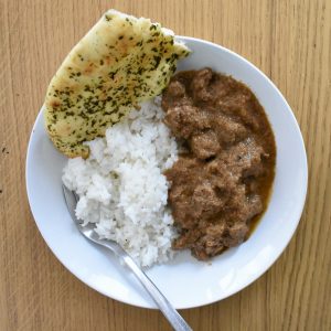 close up of served lamb rogan josh in bowl with rice and naan