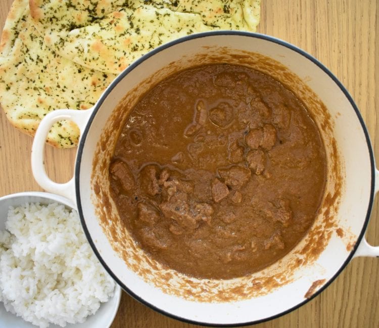 lamb rogan josh in cooking dish, naan and rice to side