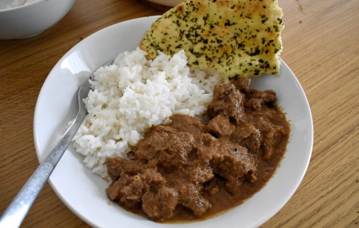 3/4 shot of lamb curry in bowl with rice and naan
