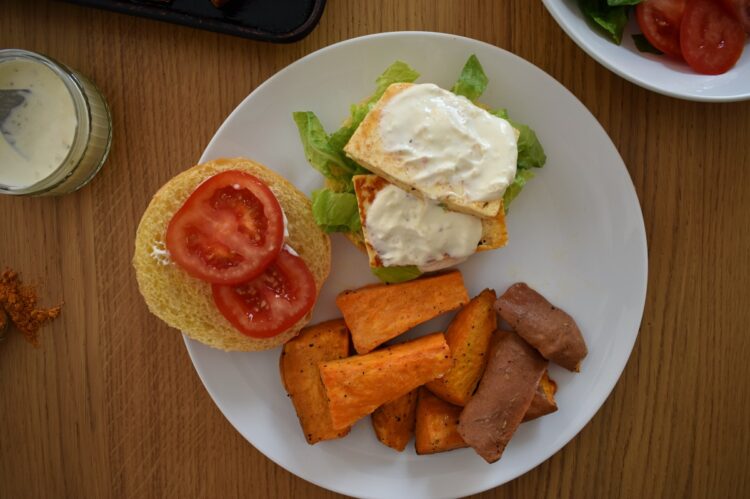 Top shot of cajun halloumi burger, with top off burger, on plate with sweet potato chips
