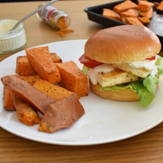 3/4 shot of served cajun halloumi burger, tray of wedges in background