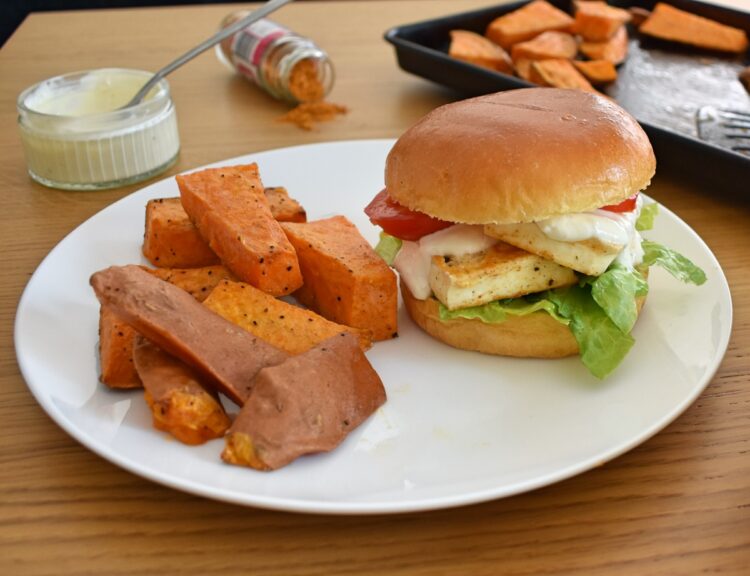 3/4 shot of served cajun halloumi burger, tray of wedges in background