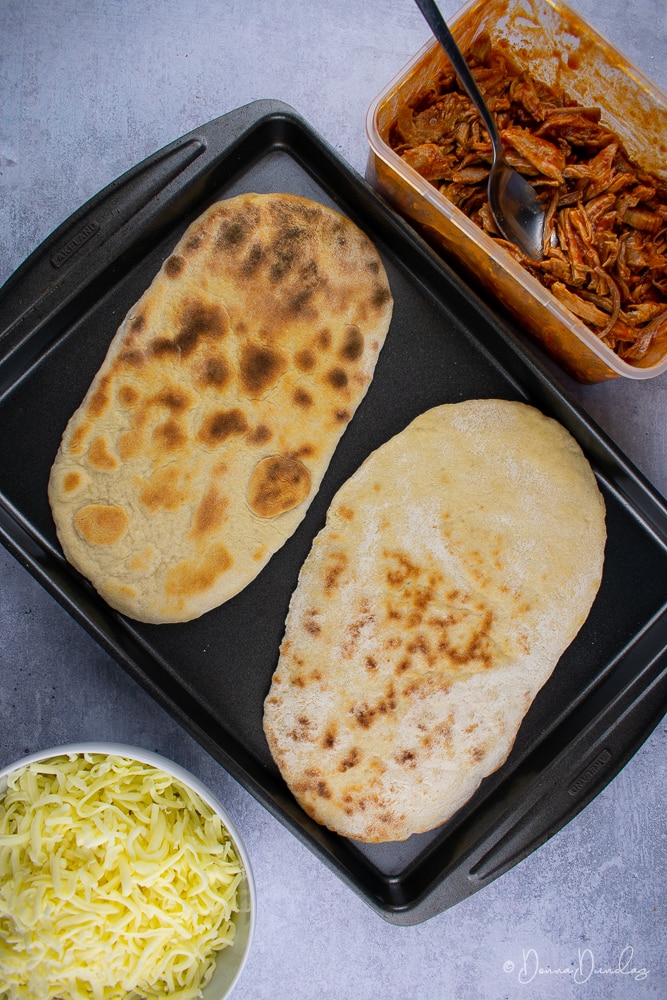 2 flatbreads on baking tray, pork and cheese to sides.
