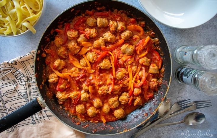 served spicy sausage pasta, frying pan and pasta bowl to the sides.