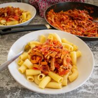 spicy leftover roast pork pasta served in bowl, frying pan in background.