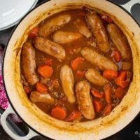 sausage and beer casserole in cast iron dish, bowl of mashed potato to the Side.
