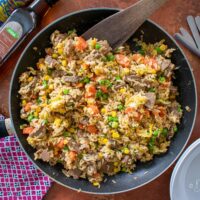 Leftover Roast Beef Fried Rice in frying pan, sesame oil, bowls and spoons to the sides.