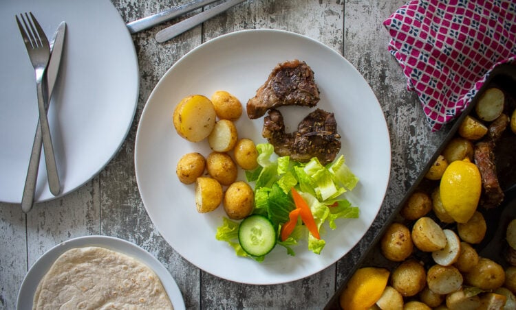 served lamb chop with potatoes and salad, baking sheet and wrap leaving the shot.