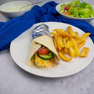 close up of inside of halloumi wrap. Halloumi, cucumber and tomato visible inside. Bowl of salad blurred in the background.