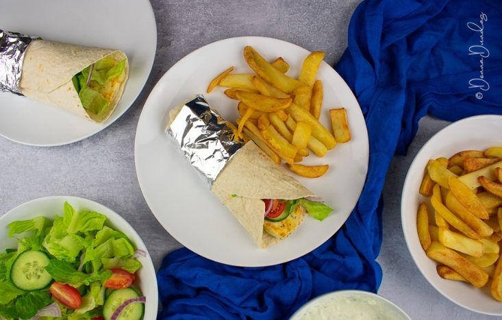Greek Halloumi Wrap on plate with chips. Bowl of chips and bowl of salad to the sides.