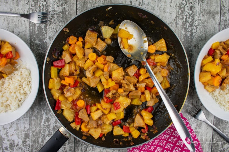 frying pan with sweet and sour pork in middle, 2 portions served with rice to the sides.