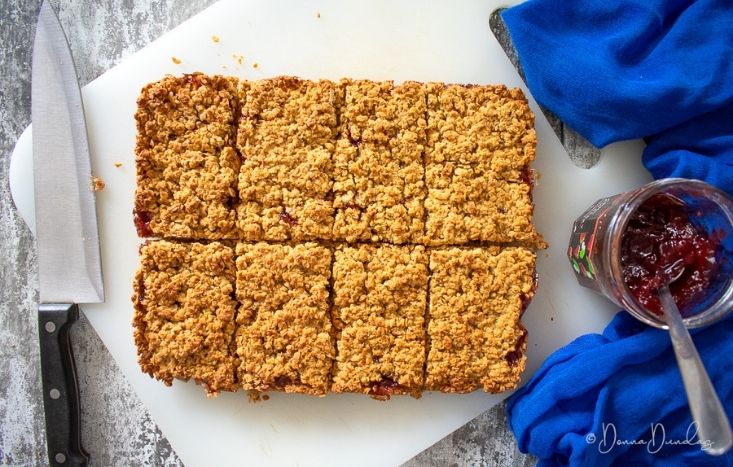 close up of flapjack on chopping board. Jar of jam to the side.