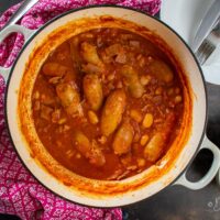 sausage and butter bean casserole in cast-iron dish, mashed potato in bowl to the side.