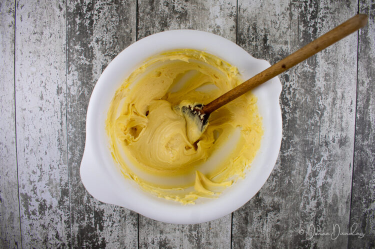 toffee buttercream icing in white mixing bowl with wooden spoon.