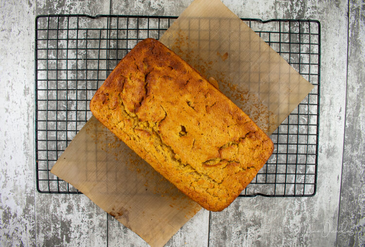 un-iced apple loaf cake on wire rack, baking paper peeled down the sides.