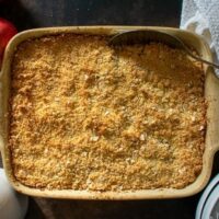 Apple and Pear Crumble in cooking pan with serving spoon. Apples and jug of custard to the sides.