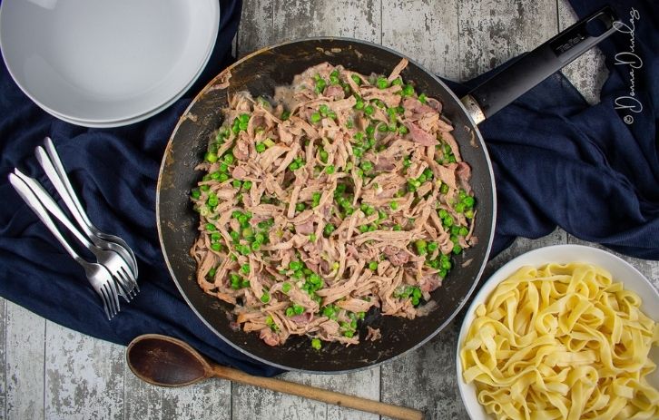 turkey in cranberry sauce with peas in frying pan. Bowl of pasta and empty pasta bowl to the sides.
