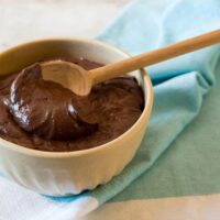 chocolate ganache in small plastic bowl with wooden spoon.