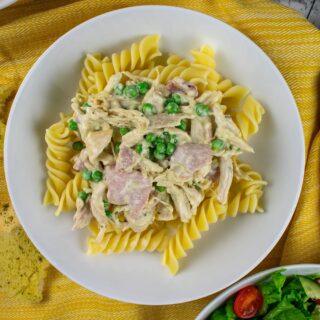 close up of served portion of leftover chicken pasta in white bowl on yellow cloth.