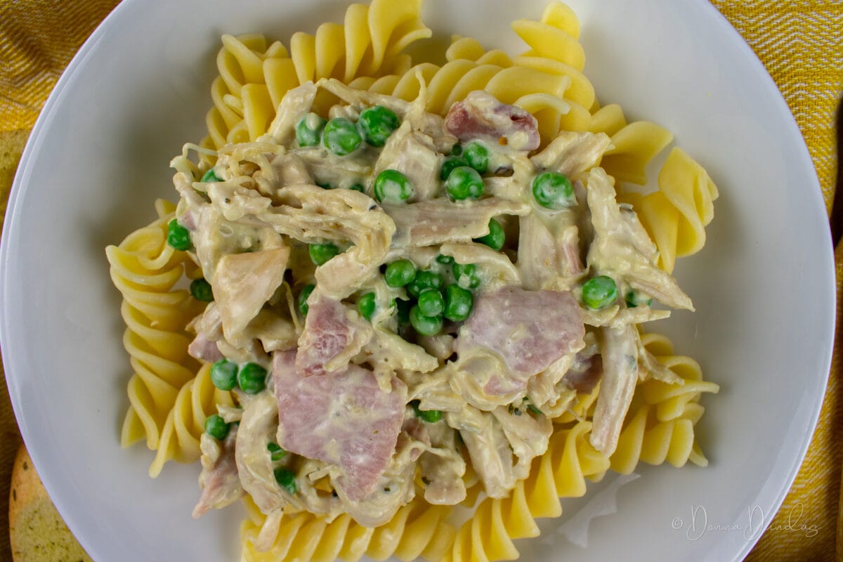 super close up of chicken and pasta with peas, bacon and cream sauce in white bowl. From above.