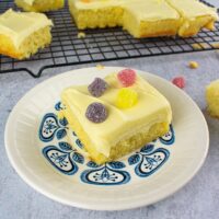 3/4 shot of square of cake with jelly tots on small plate with blue pattern. more cake cut on wire rack in the background.