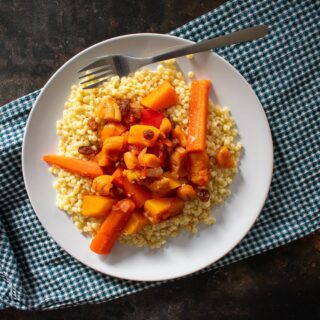 top view of served vegetable tagine with giant couscous on white plate with fork.