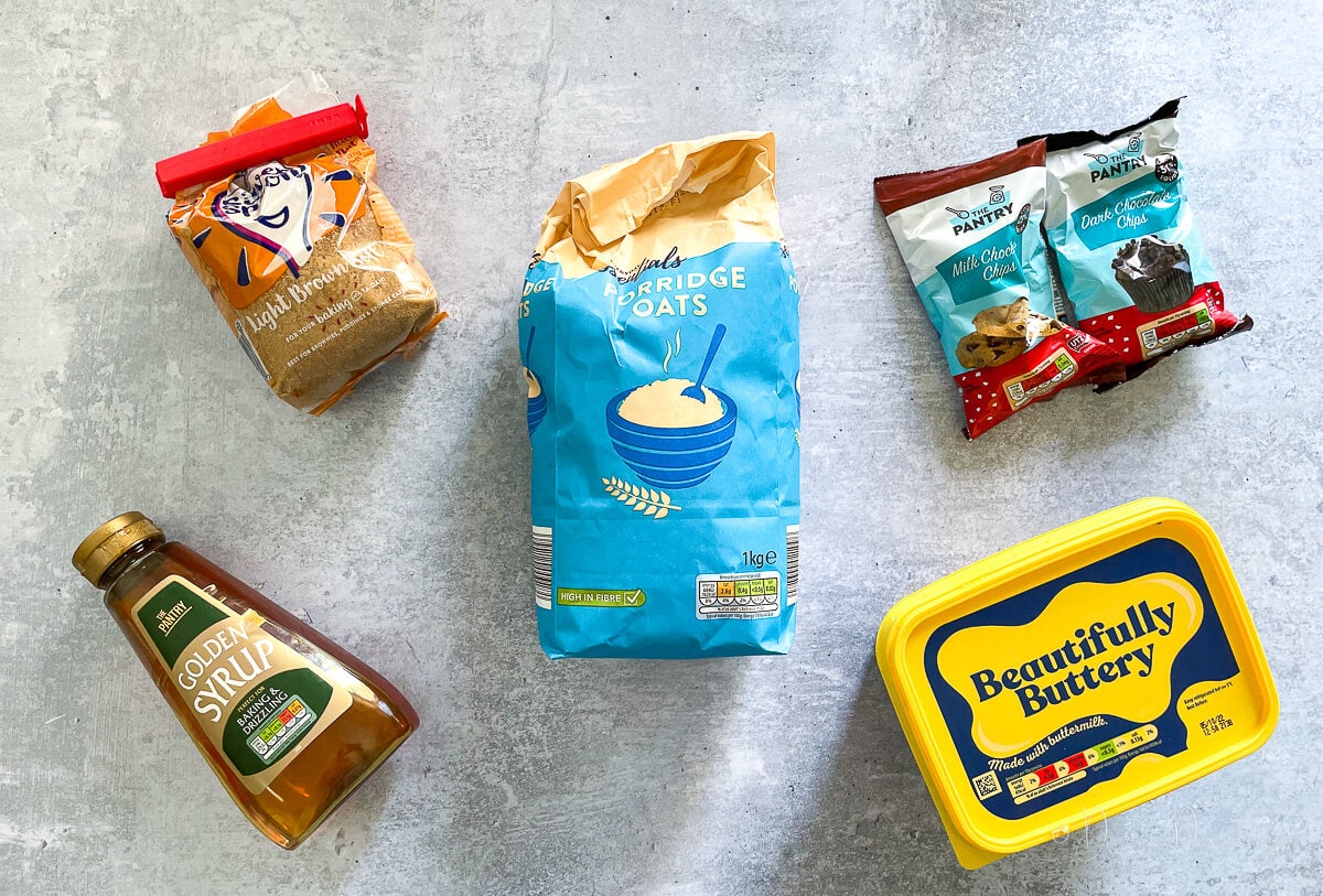 ingredients for flapjacks on table - margarine, chocolate chips, oats, light brown sugar and golden syrup.