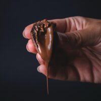 nutella ganache dripping off a piece of cake in hand. Black background.