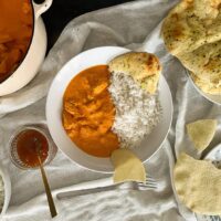 Served portion of butter turkey curry in white bowl with rice. naan bread and poppadom also in shot.