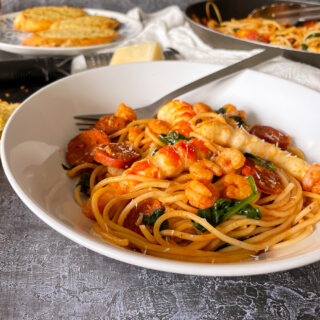 served portion of prawn and chorizo pasta in white pasta bowl with fork.