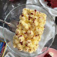 top view of red velvet loaf cake on glass cake stand. Slice of cake on plate to the side.