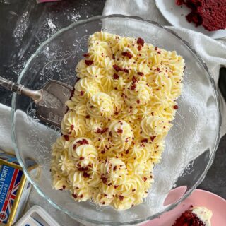 top view of red velvet loaf cake on glass cake stand. Slice of cake on plate to the side.