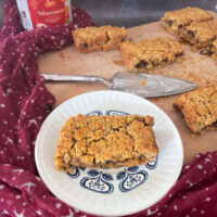slice of mincemeat flapjack on a blue and white patterned plate. Rest of flapjack sliced on chopping board with silver cake slice.