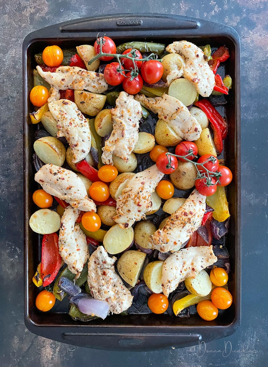traybake with peri peri chicken, potatoes, peppers, tomatoes and onion on baking tray.