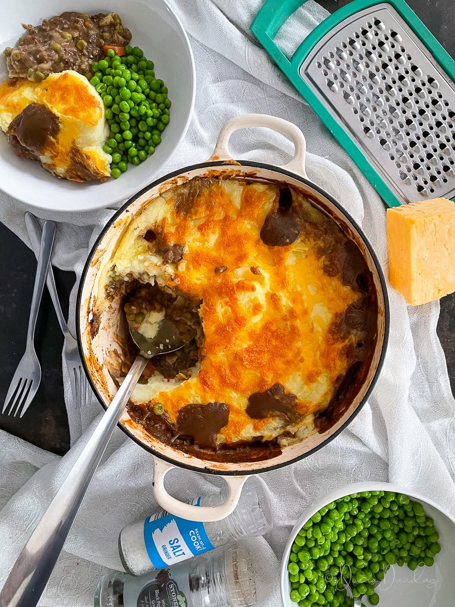 Haggis cottage pie in cast iron baking dish. Served portion and bowl of peas to the side.