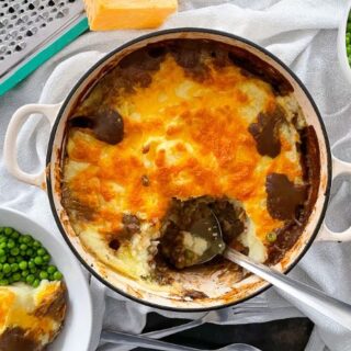 Haggis cottage pie in cast iron baking dish. Served portion and bowl of peas to the side.