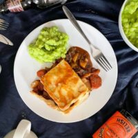Portion of leftover roast beef pie with shortcrust pastry served on a white plate with mushy peas.
