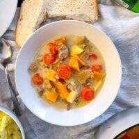 top view of a served bowl of casserole with pork, apples, carrots and swede. Apples, bowl of mash and bread also on the table.