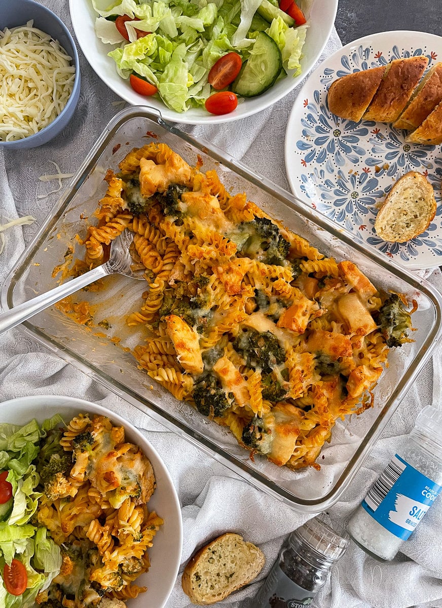 chicken and broccoli pasta bake in large glass cooking dish with serving spoon.
