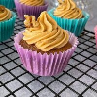 close up of coffee cake topped with icing and walnut on wire rack.