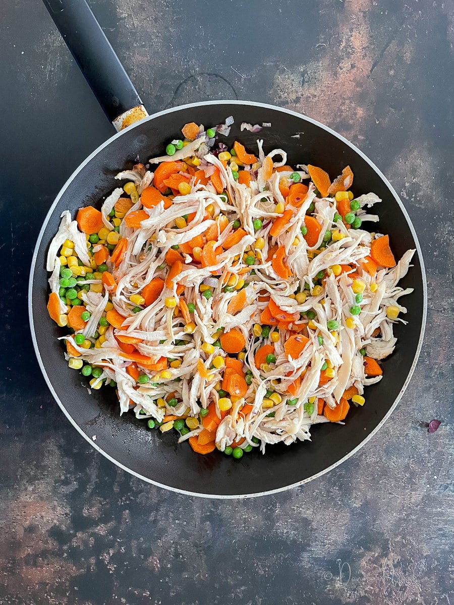 shredded cooked chicken, carrots, peas and corn in large frying pan.