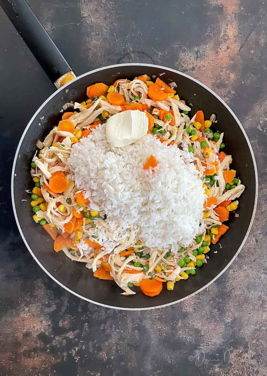 shredded chicken, peas, corn, carrots, white rice and butter in large frying pan.