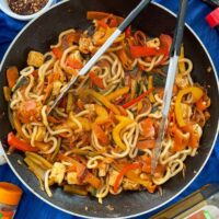 udon noodles, peppers, carrots and halloumi in a large frying pan with stir fry sauce. Soy sauce, chilli and other spices also on table.