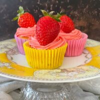 cupcakes topped with strawberries in colourful cake cases on yellow vintage cake stand.