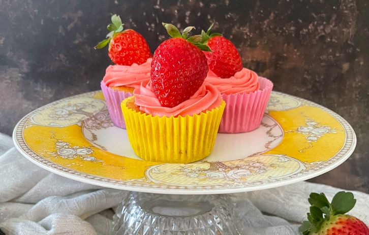 cupcakes topped with strawberries in colourful cake cases on yellow vintage cake stand.
