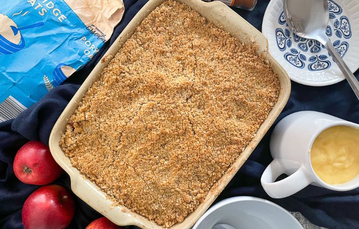 baked crumble in cooking dish. Apples, oats and custard jug also on the table.