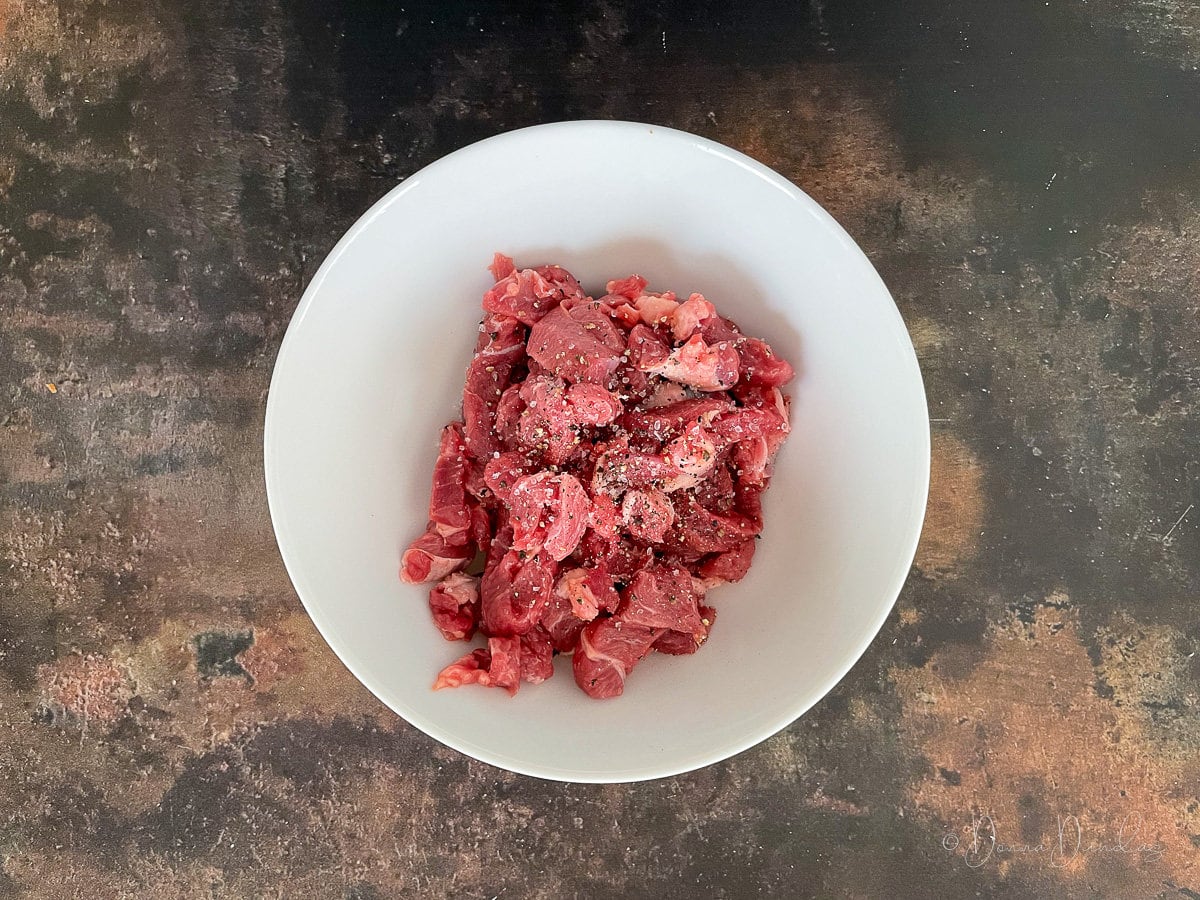 sliced uncooked lamb seasoned with salt and pepper in white bowl.
