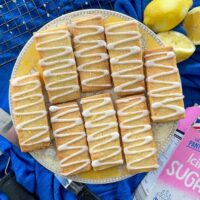 Lemon shortbread biscuits with zigzag icing on cake stand. Lemons and icing sugar also on table.